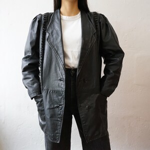 May include: A black leather blazer with a notched collar, two front pockets, and a double-breasted closure. The blazer has padded shoulders and a longline silhouette. The sleeves have a unique braided detail.