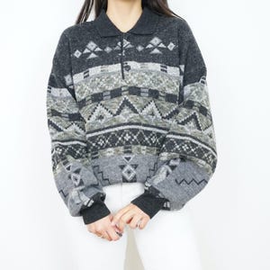 Könnte beinhalten: Ein grauer und schwarzer Pullover mit Kragen und Knöpfen. Der Pullover hat ein geometrisches Muster mit verschiedenen Formen und Farben.