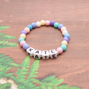 May include: A pastel-colored beaded bracelet with the name "KATE" spelled out in white letter beads.