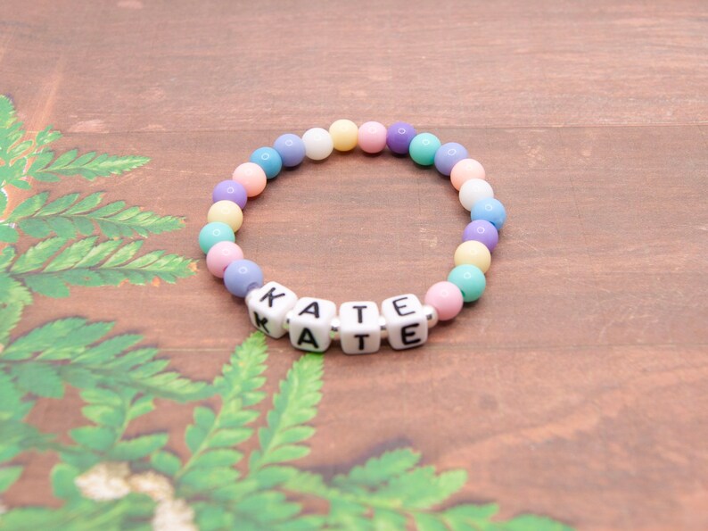 May include: A pastel-colored beaded bracelet with the name "KATE" spelled out in white letter beads.