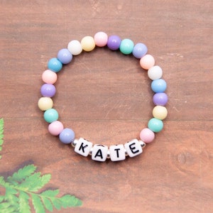 May include: A pastel-colored beaded bracelet with the name "KATE" spelled out in white letter beads.