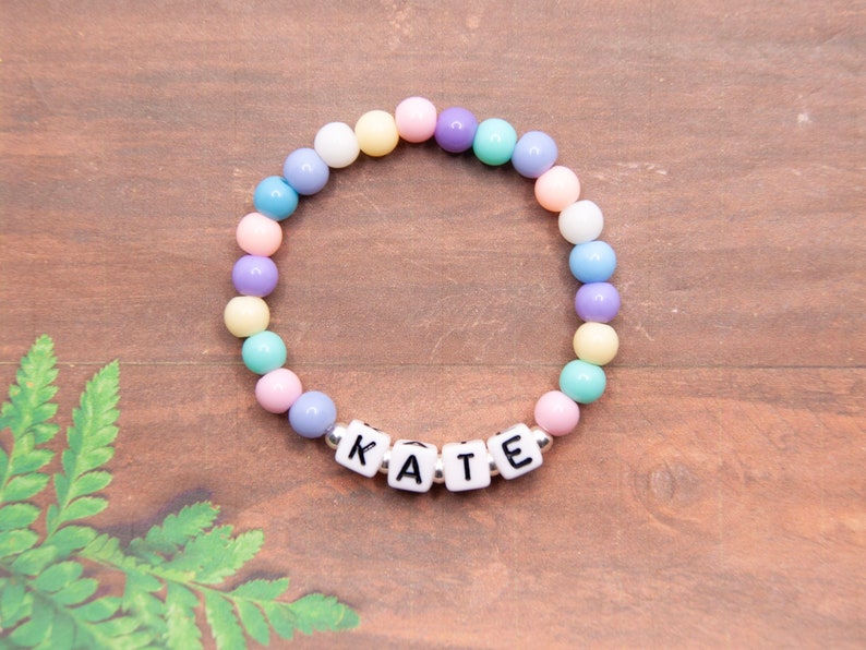 May include: A pastel-colored beaded bracelet with the name "KATE" spelled out in white letter beads.