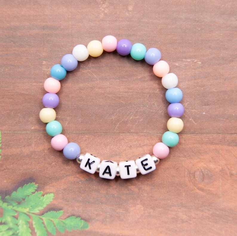 May include: A pastel rainbow beaded bracelet with the name "KATE" spelled out in white letter beads.