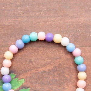 May include: A pastel-colored beaded bracelet with alternating shades of light blue, pink, yellow, and purple.