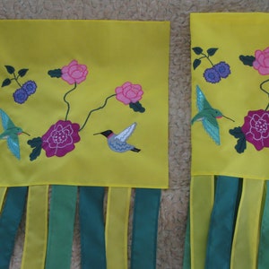 May include: Two yellow fabric panels with embroidered hummingbirds, flowers, and leaves. The panels have green and yellow fringe at the bottom.