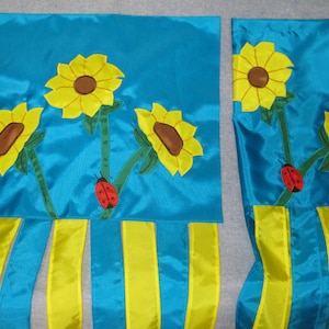 May include: Two blue fabric panels with yellow and green embroidered sunflowers and ladybugs. The panels have yellow ribbon tails.