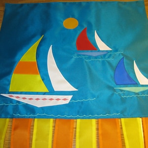 May include: A blue fabric banner with a yellow sun and four sailboats in different colors. The banner has orange and yellow fringe at the bottom.