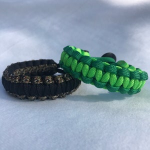 May include: Two paracord bracelets, one black and green camouflage, the other green and lime green.