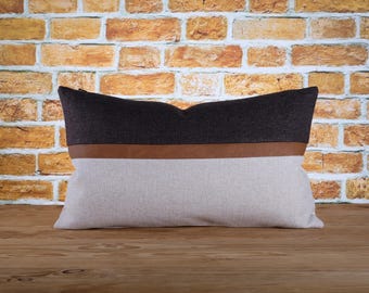 Könnte beinhalten: Ein Dekokissen mit einem braunen Lederstreifen und einem schwarzen und weißen Stoffdesign.