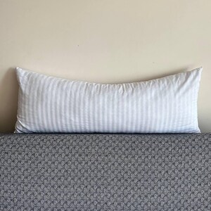 May include: A white and gray striped body pillow with a soft, plush texture. The pillow is lying on a black and white patterned surface.