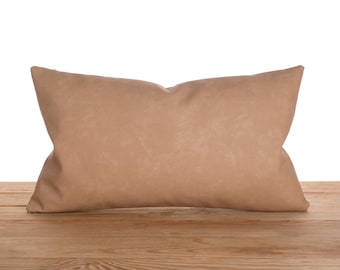 Puede incluir: Una almohada rectangular de color marrón claro con una superficie suave y texturizada. La almohada está sobre una superficie de madera.