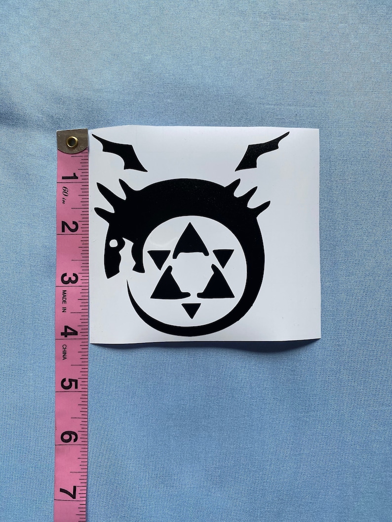 May include: A black vinyl sticker featuring a circular design with a dragon-like creature, a six-pointed star, and a crescent moon. The sticker is approximately 3 inches (7.6 cm) in height and width.