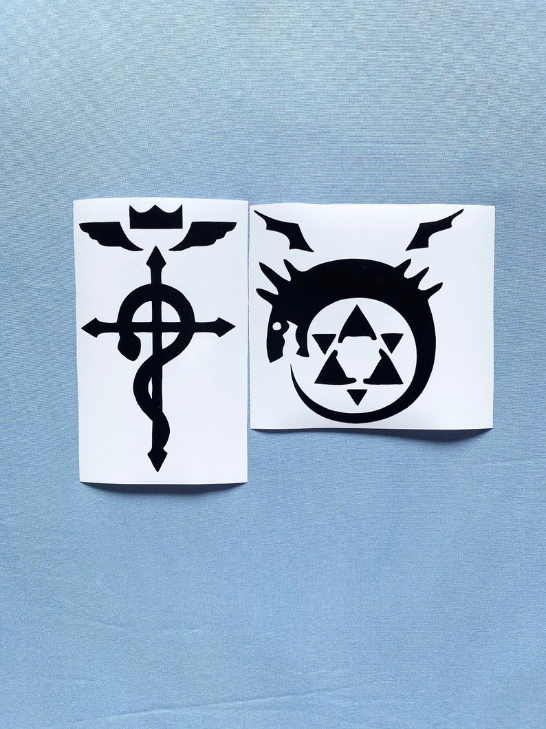 May include: Two black and white stickers. One features a cross with a snake wrapped around it, wings, and a crown. The other sticker has a dragon-like creature inside a circle with a star and triangles.
