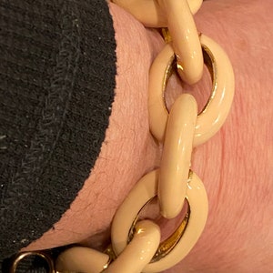 May include: Cream-colored chain link bracelet with gold-tone accents. The bracelet features large, oval links in a glossy finish. The clasp is gold-toned. A stylish accessory.