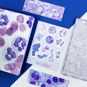 May include: A collection of stationery items featuring a watercolor design of cells in shades of purple and white. Includes a notebook, stickers, a notepad with the text "LET'S GO!", and two rectangular cards. The items are arranged on a blue and white surface.