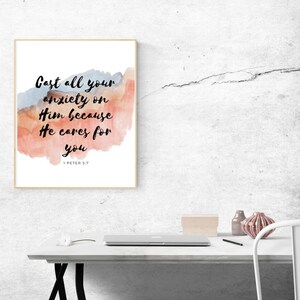 May include: A framed print with a watercolor background in shades of pink, orange, and blue. The print features the text "Cast all your anxiety on Him because He cares for you" with the scripture reference "1 Peter 5:7" below.