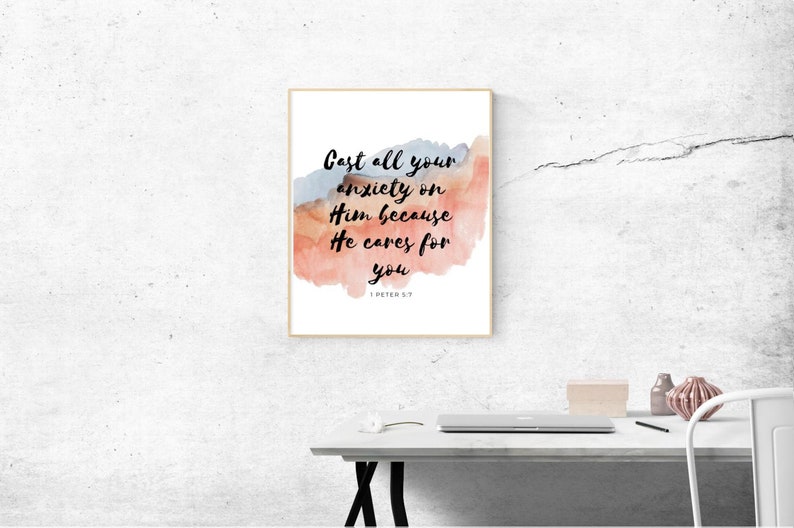 May include: A framed print with a watercolor background in shades of pink, orange, and blue. The print features the text "Cast all your anxiety on Him because He cares for you" with the scripture reference "1 Peter 5:7" below.