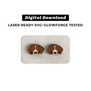Pode incluir: Dois brincos de madeira marrom em forma de cabeça de cachorro com marcas brancas e olhos laranja. LASER READY SVG | GLOWFORGE TESTED.