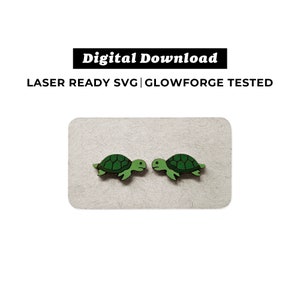 Może przedstawiać: Dwa zielone drewniane kolczyki w kształcie żółwia na białym tle. Żółwie patrzą na siebie. Tekst "Pobierz cyfrowo" znajduje się nad żółwiami, a tekst "LASER READY SVG | GLOWFORGE TESTED" pod żółwiami.