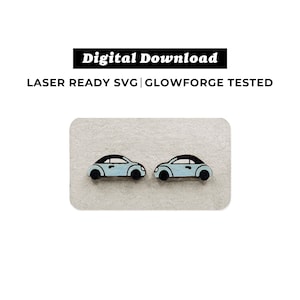 May include: Two light blue wooden car earrings with black details. The earrings are displayed on a light brown surface.