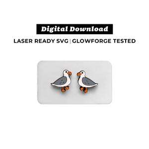 May include: A pair of wooden seagull earrings. The earrings are gray and white with orange beaks and feet. The earrings are on a white background.
