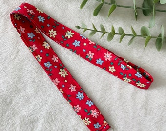 May include: A red lanyard with a floral pattern and a silver swivel clip. The lanyard is made of fabric and has a repeating pattern of small flowers in shades of pink, blue, and yellow.