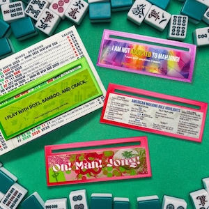 May include: A selection of Mahjong game components, including tiles and rule cards. The cards display phrases such as "I play with dots, bamboo, and crack" and "I am not addicted to Mahjong!" The game pieces are on a green surface.