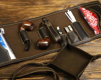 May include: A brown leather roll-up case with multiple pockets and compartments. The case contains two pipes, a small tool, and a small pouch. The case is open and laid flat on a wooden surface.