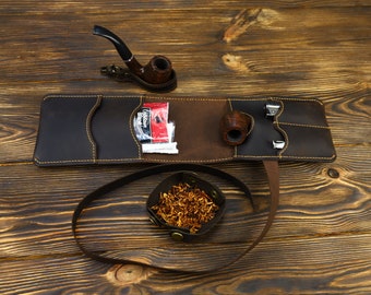 May include: A brown leather tobacco pouch with a pipe, tobacco, and a pipe tool. The pouch has a strap and is open to reveal the contents. A small bowl of tobacco is also visible.