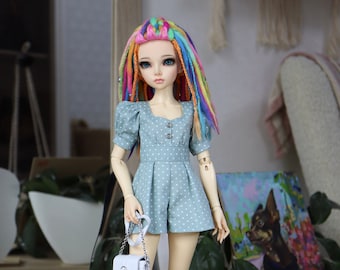 May include: A doll with long, rainbow-colored hair wearing a light blue polka dot dress and white sandals. The doll is holding a white purse with a gold chain.