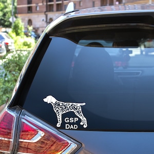 May include: A white car with a black and white dog silhouette sticker on the back window. The sticker says "GSP DAD".
