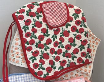 May include: A collection of quilted fabric bibs featuring various patterns including red tomatoes with green leaves, pink strawberries, blue and white plaid, and green stripes. Each bib has a soft quilted texture and colourful fabric trim edges.