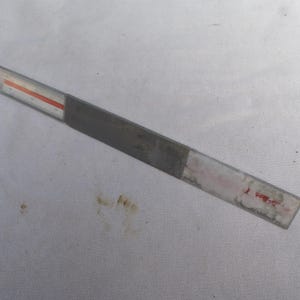 Puede incluir: Una regla de metal gris con una franja roja y blanca en la parte superior. La regla mide aproximadamente 30 cm de largo.