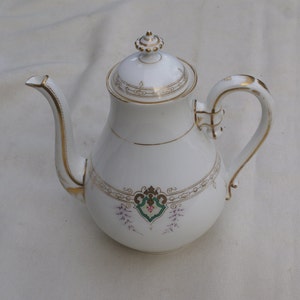 以下が含まれることがあります： 金色の縁取りと花柄の白い磁器製のティーポット。ティーポットは、上にノブが付いた蓋が付いています。