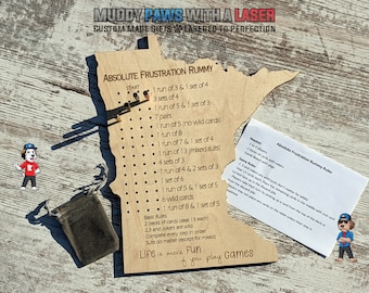 Puede incluir: Un tablero de juego de madera con forma del estado de Minnesota con el título "Absolute Frustration Rummy". El tablero tiene una lista de combinaciones de rummy para completar, como "1 run of 3 & 1 set of 4", "3 sets of 4" y "1 run of 5 & 1 set of 3". El tablero está hecho de madera marrón claro y tiene un acabado natural. Una pequeña bolsa marrón está al lado del tablero, y una hoja de papel blanca con las reglas del juego está a la derecha del tablero.