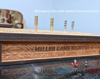 Puede incluir: Un tablero de cribbage de madera con clavijas doradas y plateadas. La caja de caoba está grabada con "MILLER GAME NIGHT" y un patrón geométrico. El texto "Mahogany Box with Added Personalization" está encima del tablero.