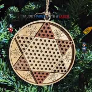 May include: A wooden Christmas ornament shaped like a star with a checkerboard pattern. The ornament is made of two different types of wood, one light and one dark. The ornament is hanging on a Christmas tree.