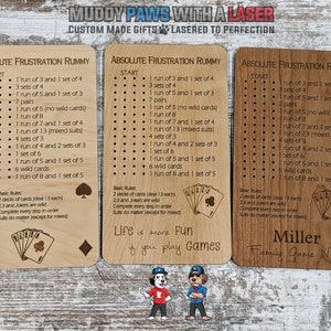 May include: Three wooden game cards with the title "Absolute Frustration Rummy" and a list of rules for the game. The cards are light brown with black text and a black and white illustration of playing cards. The bottom card has the text "Miller Family Game Night".