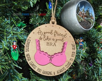 Puede incluir: Un adorno redondo de madera con un recorte de sujetador rosa y el texto "A good friend is like a good BRA SUPPORTIVE NEVER LEAVES YOU HANGING & ALWAYS CLOSE TO YOUR HEART".