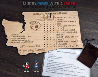 Puede incluir: Tablero de juego de madera con forma del estado de Washington con el texto "Absolute Frustration Rummy" y una lista de reglas para el juego. El tablero tiene clavijas y agujeros para jugar al juego. El juego está hecho por Muddy Paws with a Laser.