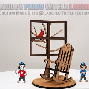 May include: A wooden rocking chair with a personalized name tag that reads "Bradley". The chair is part of a wooden window scene with a red cardinal perched on a branch. The scene is on a wooden base with a dog mascot on either side.