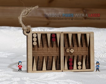 Puede incluir: Un adorno de juego de backgammon de madera con fichas rojas y blancas. El adorno tiene la forma de una pequeña caja con una tapa con bisagras. El adorno está hecho por Muddy Paws With A Laser, una empresa que hace regalos personalizados.