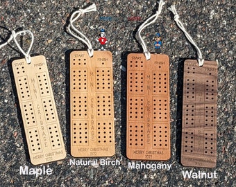 Puede incluir: Cuatro mini tableros de cribbage de madera en diferentes acabados: arce, abedul natural, caoba y nogal. Cada tablero tiene las palabras "MINI CRIBBAGE" y "FELIZ NAVIDAD 2022" grabadas.
