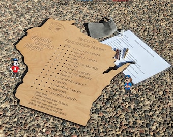 Puede incluir: Un tablero de juego de madera con forma del estado de Wisconsin con las palabras "Family Game Night" y "Absolute Frustration Rummy" impresas en él. El tablero tiene una lista de reglas para el juego, incluyendo el número de conjuntos y carreras de cartas necesarias para ganar.
