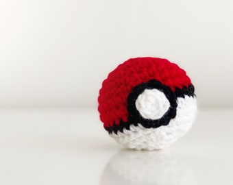 May include: A crocheted red and white ball with a black circle in the centre. The ball is a replica of a Poké Ball.