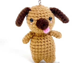 May include: A brown crocheted dog keychain with brown ears, a brown nose, and pink tongue. The dog has black eyes and pink cheeks.