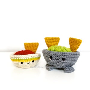 May include: Two crocheted food bowls with smiling faces. One bowl is white with red filling and yellow and green stripes, the other is gray with green filling. Both have yellow triangle chips.