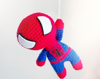 May include: A crocheted Spiderman toy with a red and blue costume. The toy has a white eye mask and a black spider logo on the chest.
