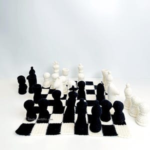 May include: A crocheted chess set with black and white pieces arranged on a checkered board. The pieces are in the traditional chess shapes. The board is a black and white checkerboard pattern.