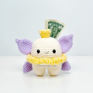 May include: A white crocheted tooth fairy with purple wings, a yellow crown, and a yellow ruffle collar. The fairy is holding a dollar bill in its hand. ©knotmonsters.com
